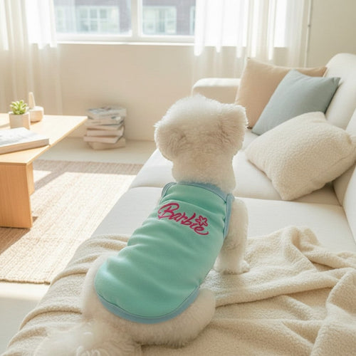 The Spoiled Pet Club dog tank top in sky blue with pink Barbie embroidery, worn by a white dog on a cozy sofa.