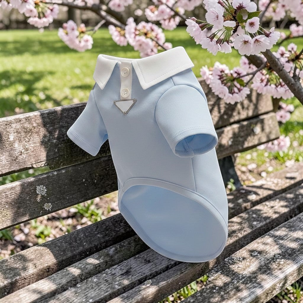 The Spoiled Pet Club light blue cotton dog polo shirt with a white collar on a wooden bench under cherry blossoms.