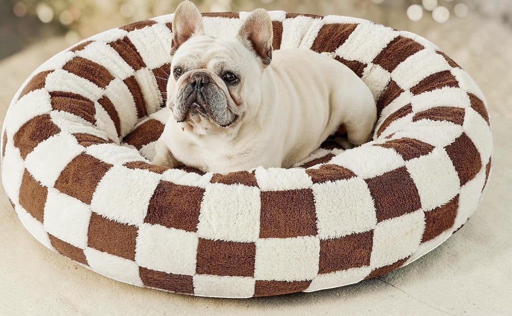 A French Bulldog resting in a round, plush pet bed with a brown and white checkered pattern by The Spoiled Pet Club.