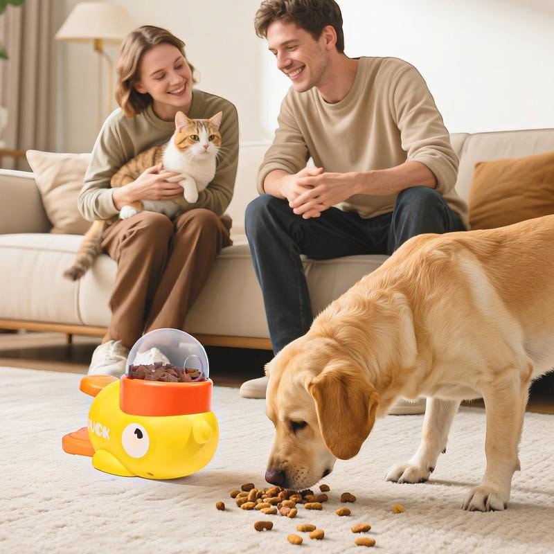 The Spoiled Pet Club yellow duck treat dispenser with a clear top filled with kibble, a dog eating kibble from the floor.
