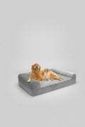 The Spoiled Pet Club gray orthopedic dog bed with plush bolster sides and a soft gray faux fur cushion. Two golden retrievers relax on the bed.
