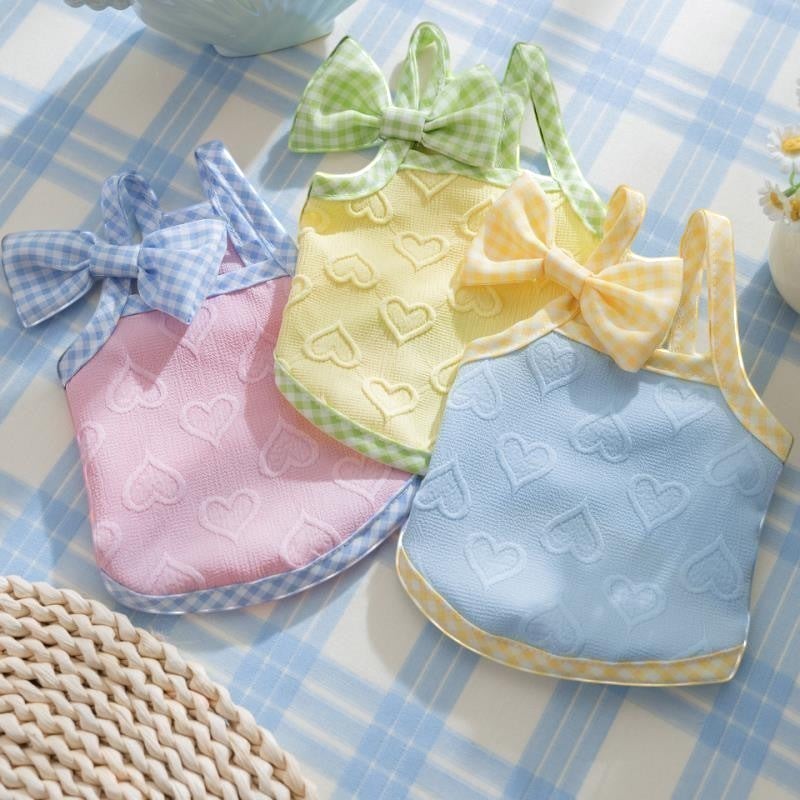The Spoiled Pet Club heart-patterned dog tank tops in pink, yellow, and blue with gingham bows on a plaid surface.