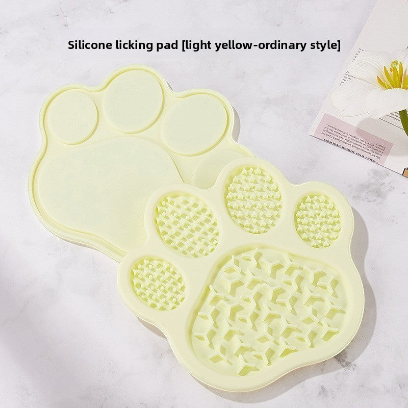 The Spoiled Pet Club paw-shaped light yellow silicone lick mat for slow feeding on a white marble surface
