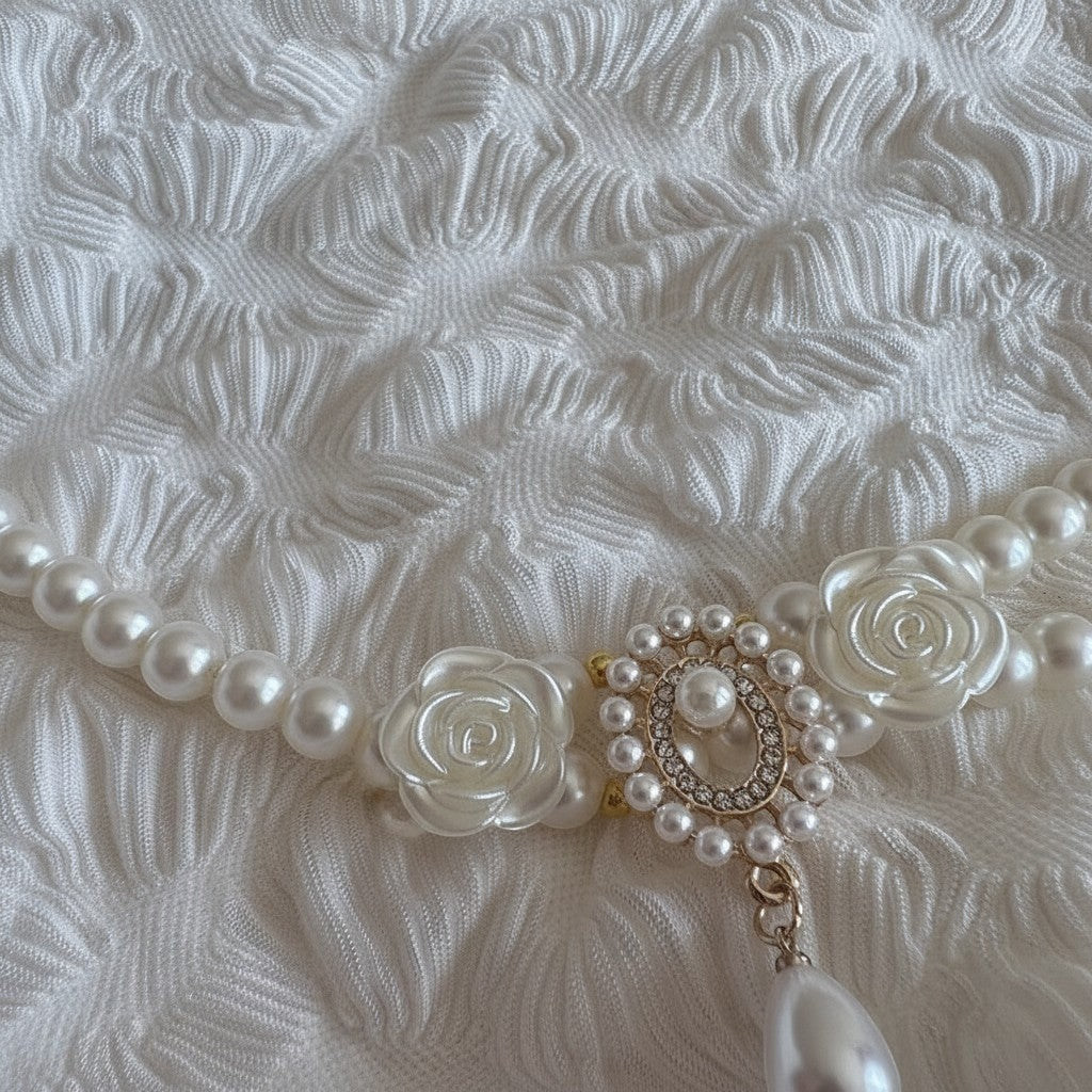 The Spoiled Pet Club vintage pearl cat collar with floral patterns and a dangling pendant on a textured white fabric.