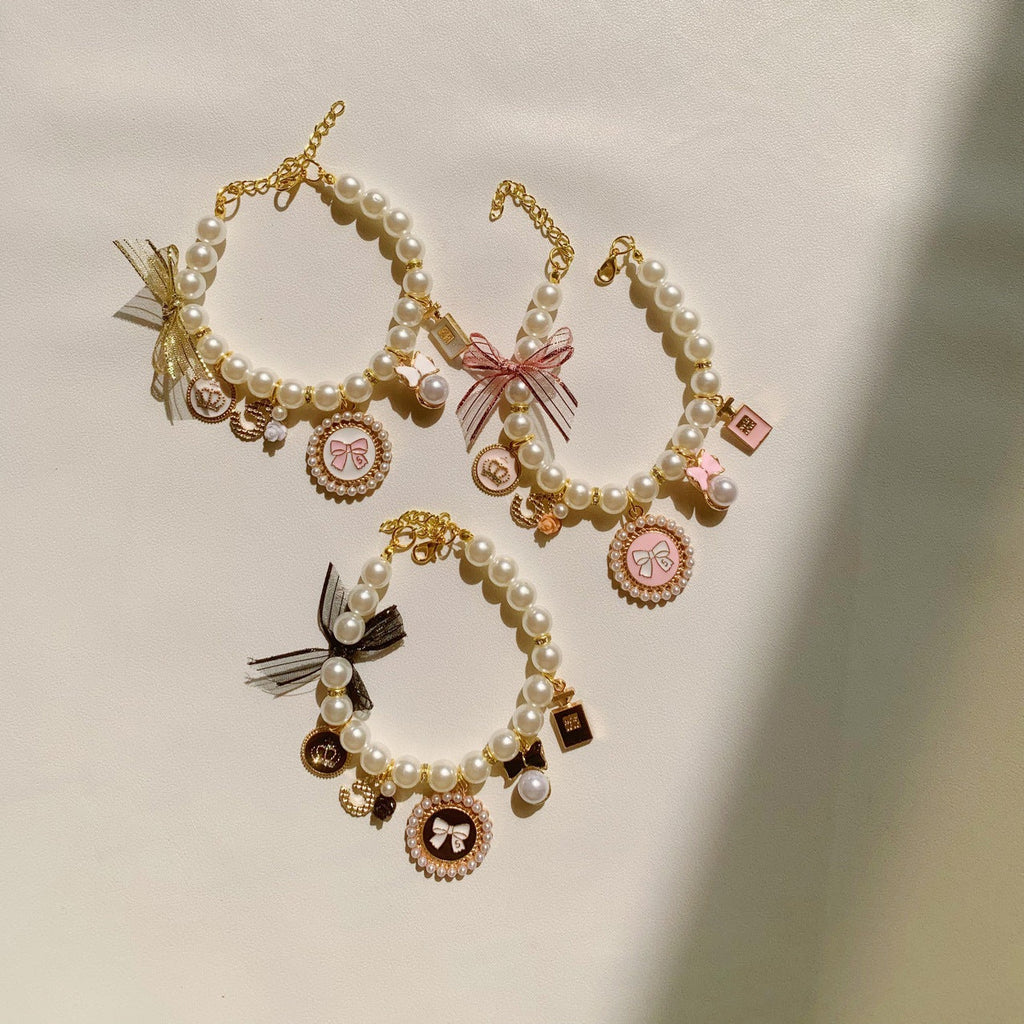 The Spoiled Pet Club pearl pet collars with bow charms, bell accents, and letter patterns in pink, black, and white.