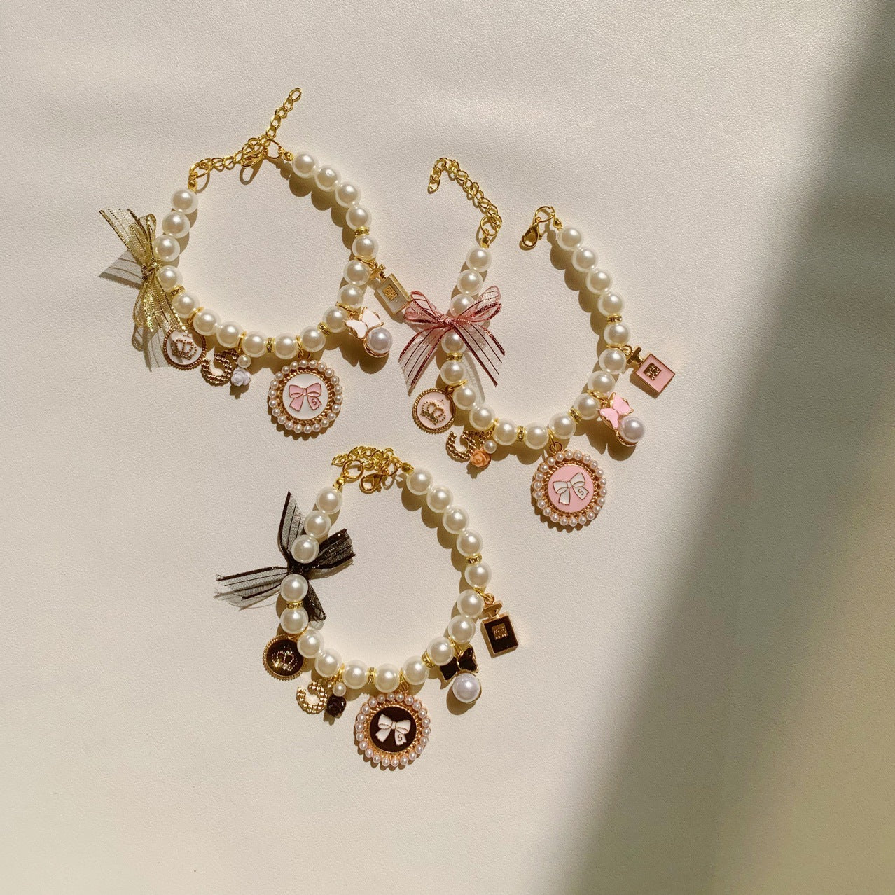 The Spoiled Pet Club pearl pet collars with bow charms, bell accents, and letter patterns in pink, black, and white.