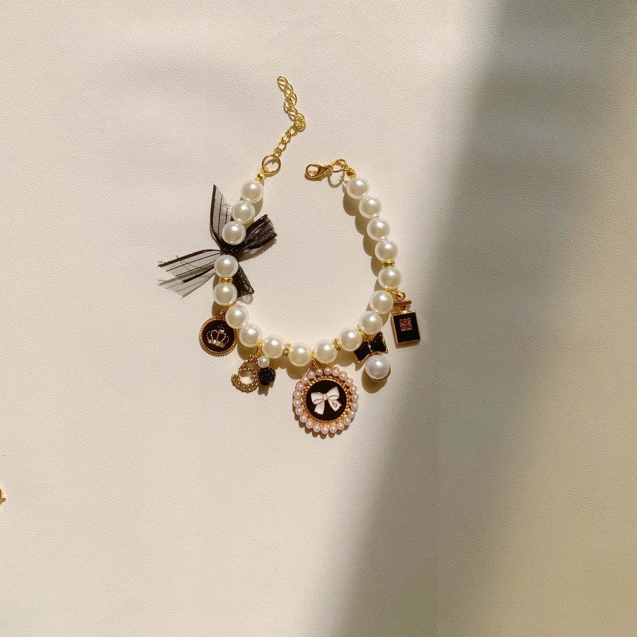 The Spoiled Pet Club pearl pet necklace featuring a black bow, gold charms, and a decorative pendant on a light background