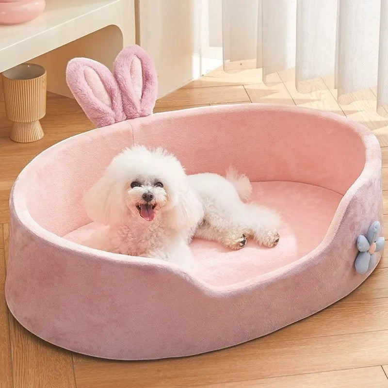 The Spoiled Pet Club pink plush dog bed with raised edges and bunny ears. Features a small blue flower accent.