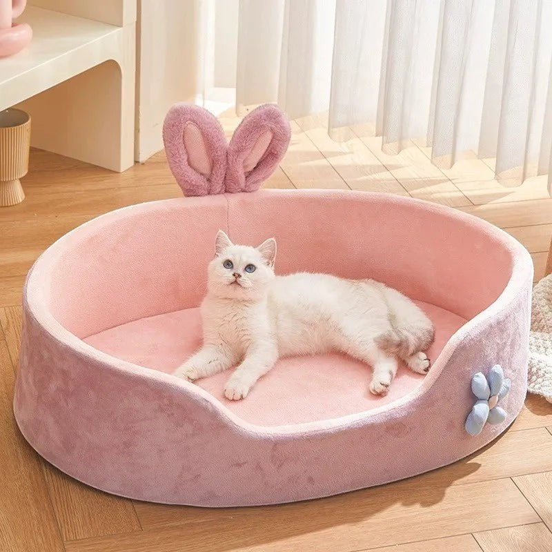 The Spoiled Pet Club pink plush cat bed with raised edges and bunny ears. Features a blue flower accent.