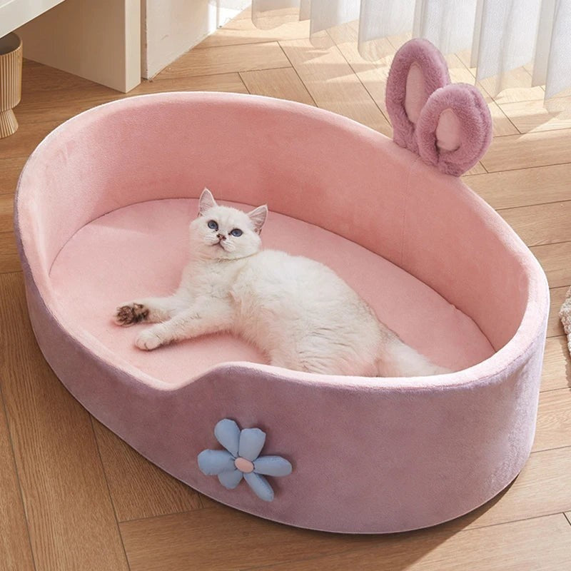 The Spoiled Pet Club pink plush pet bed with raised edges, bunny ears, and flower accent. White cat lounging inside.