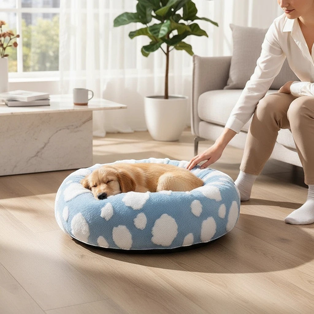 The Spoiled Pet Club round blue pet bed with white cloud pattern, featuring a sleeping puppy in a cozy living room.