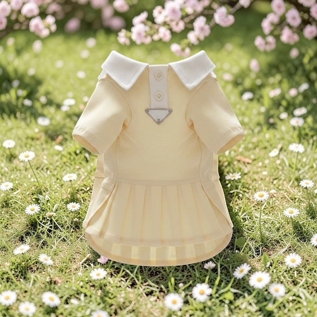 The Spoiled Pet Club yellow cotton dog dress with a white polo collar, button placket, and pleated skirt in a garden.